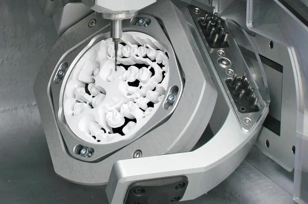 Five-axis mill mid-cut on a zirconia disc, restorations nested in the puck