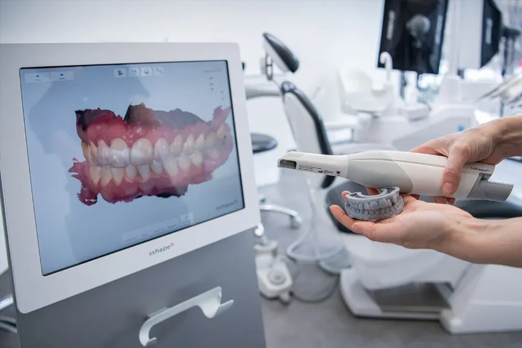 Intraoral scanner in hand beside a monitor showing a 3D digital arch