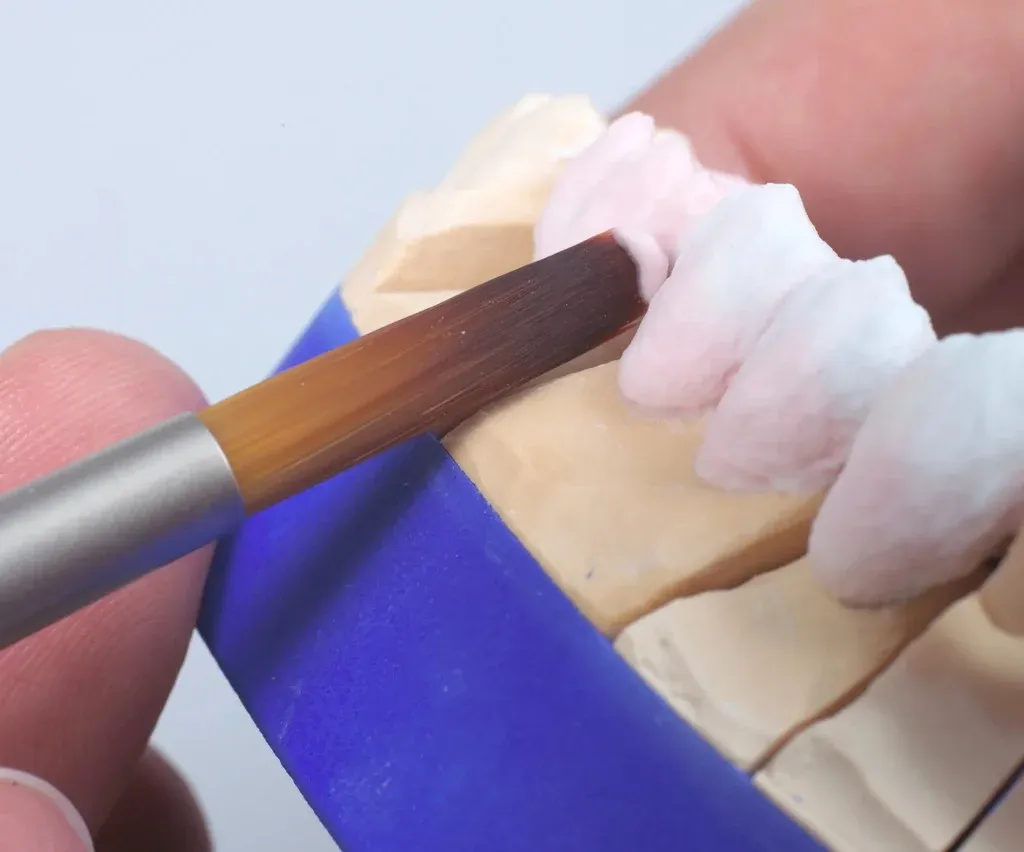 A ceramist layering feldspathic porcelain over a milled zirconia coping